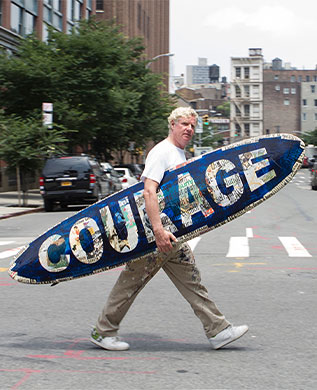 Man with surfboard that says courage on the surface